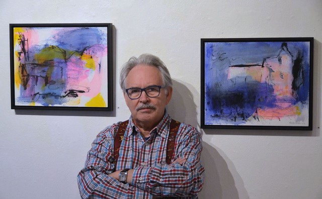 Konstnär Åke Bjurhamn står framför två av sina tavlor